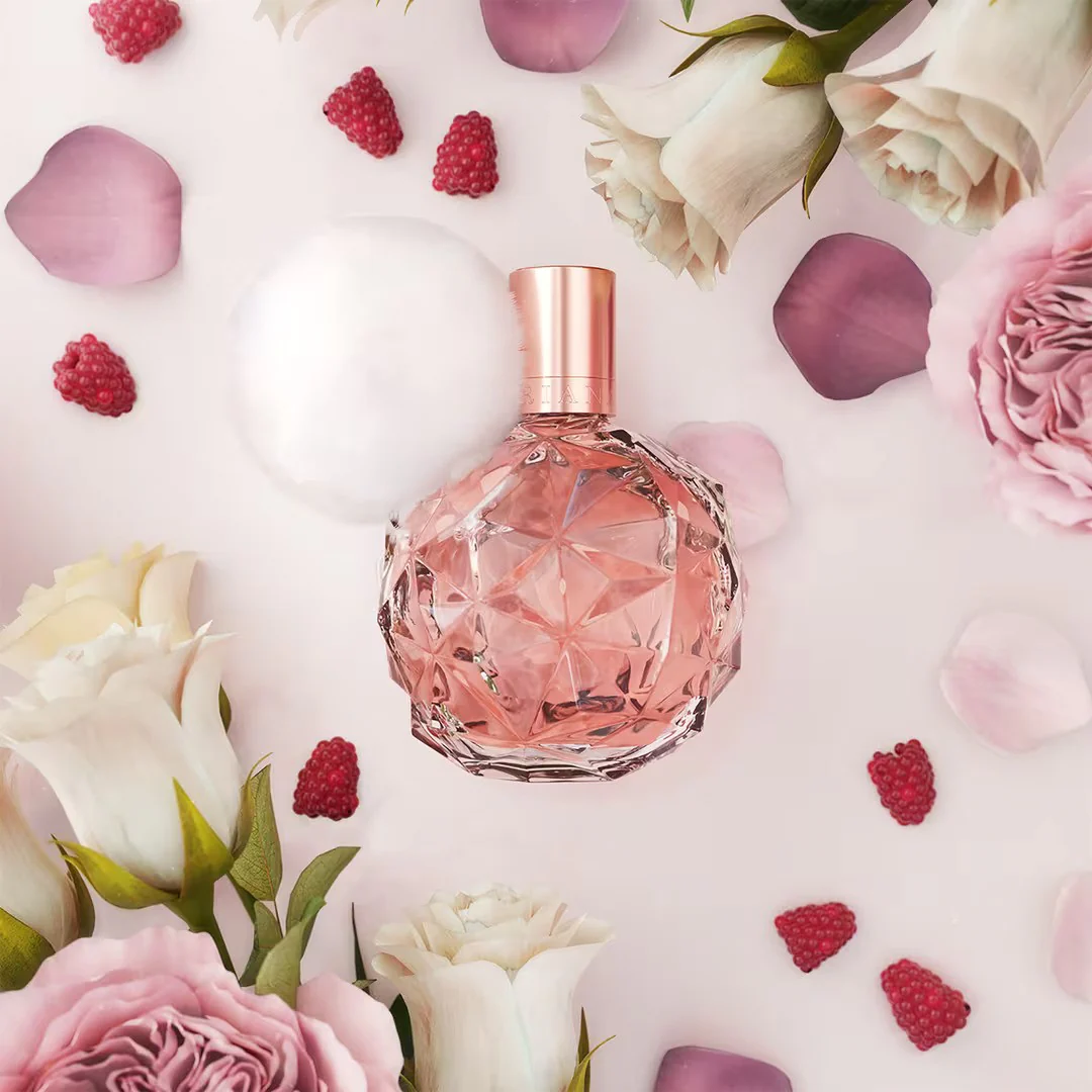 ari by ariana grande » Scott Beauty Shop Pink crystal perfume bottle nestled among white and pink roses with scattered petals on a pale background.